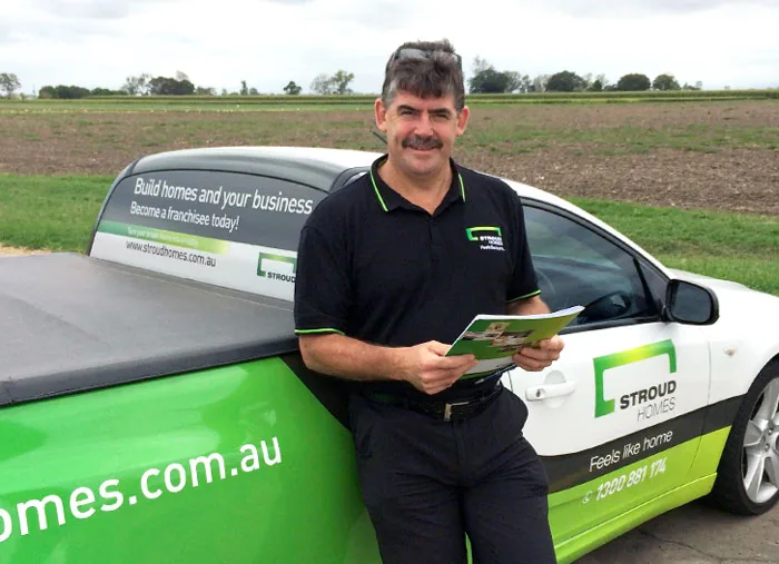A Stroud Homes builder holding a brochure beside a branded ute and car